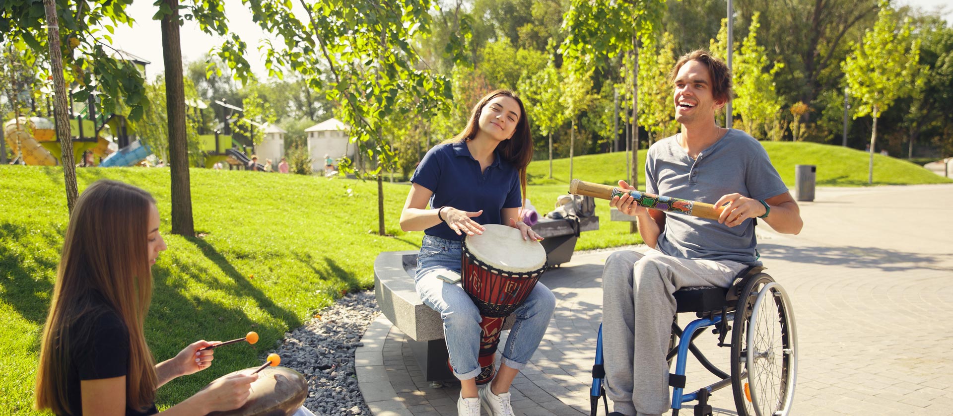 Two women playing hide drums with a man in a wheelchair who is playing a maraca-style instrument.
